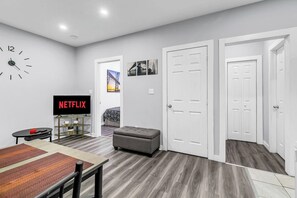 A modern living room with a flat-screen TV, a clock, a dining table, and a sofa. - Modern & Private 1-Bedroom Apartment (Windsor)