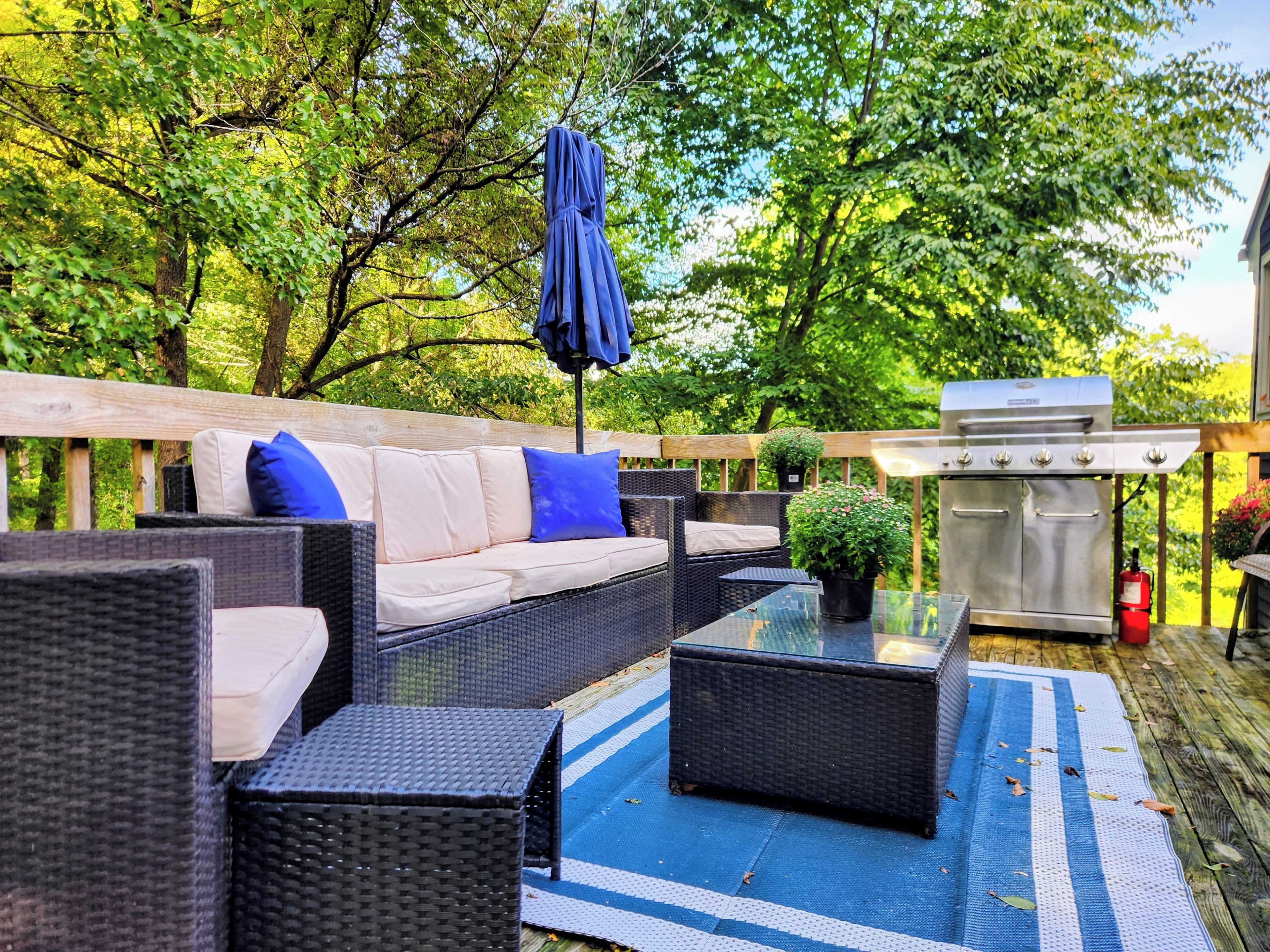Eine Terrasse im Freien mit Korbmöbeln, einem Glastisch und einem Grill.