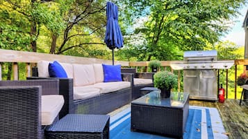 Eine Terrasse im Freien mit Korbmöbeln, einem Glastisch und einem Grill.