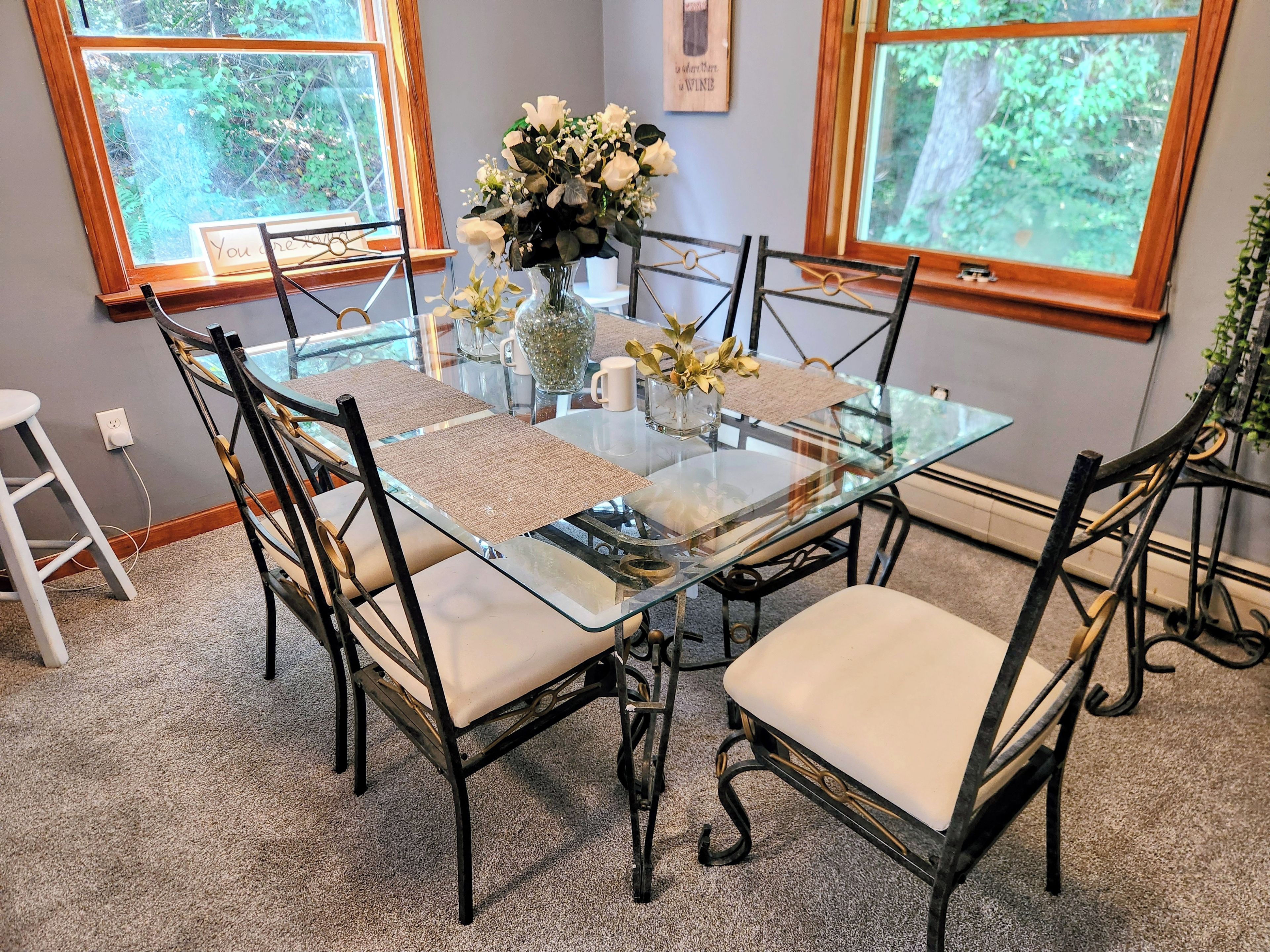 A glass-top dining table with four chairs, a vase with flowers, and a framed picture on the wall.