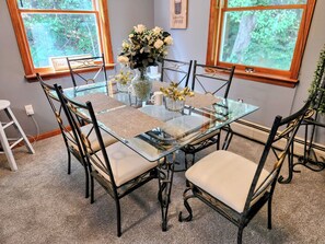 A glass-top dining table with four chairs, a vase with flowers, and a framed picture on the wall.