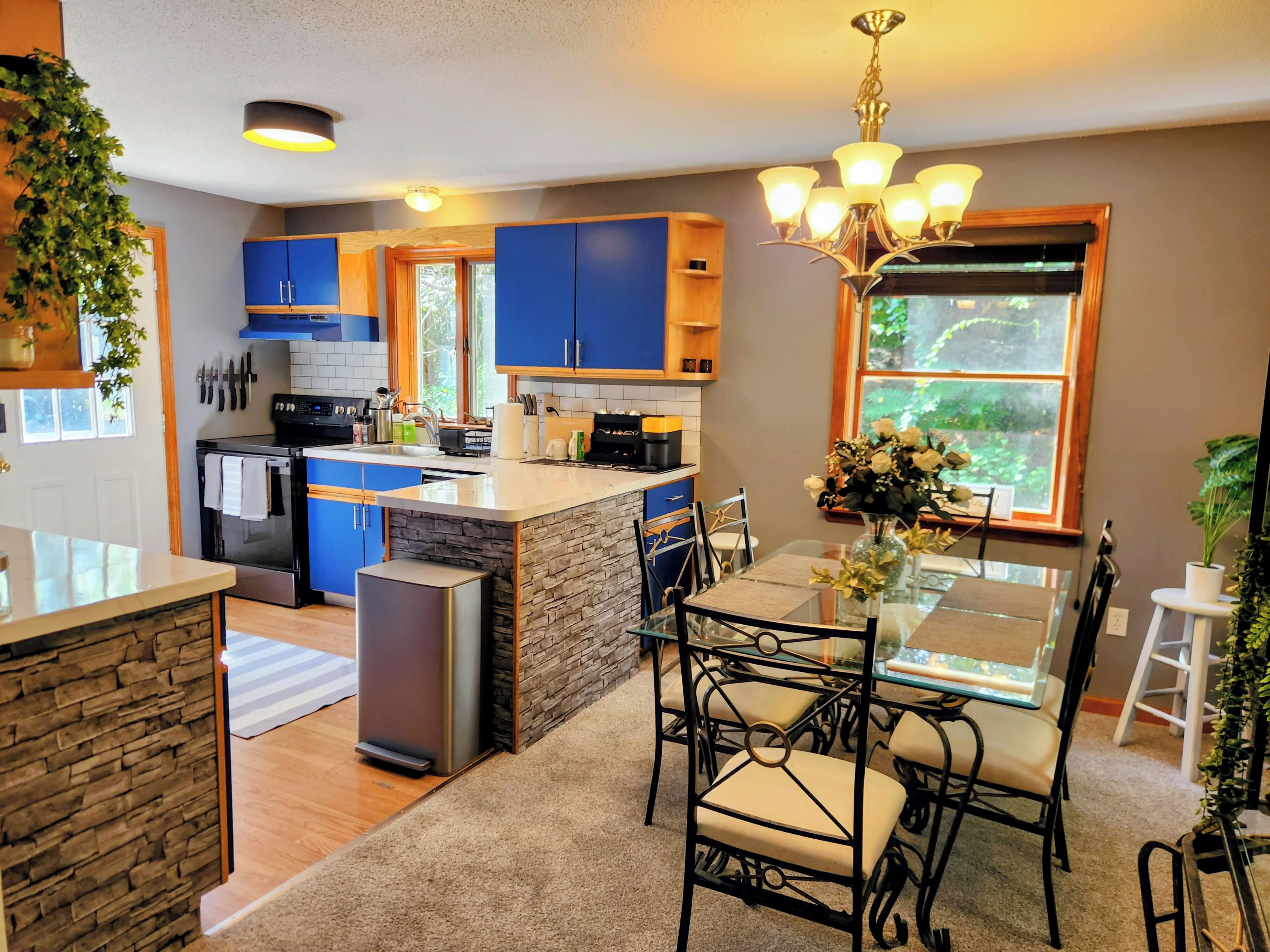 A modern kitchen with blue cabinets, a central island, and a dining area with a glass table and chairs.