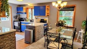 Una cocina moderna con armarios azules, una isla central y un comedor con mesa y sillas de vidrio.