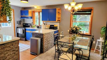 A modern kitchen with blue cabinets, a central island, and a dining area with a glass table and chairs.