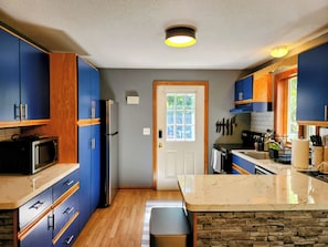 A modern kitchen with blue cabinets, a marble countertop, and a stone backsplash.