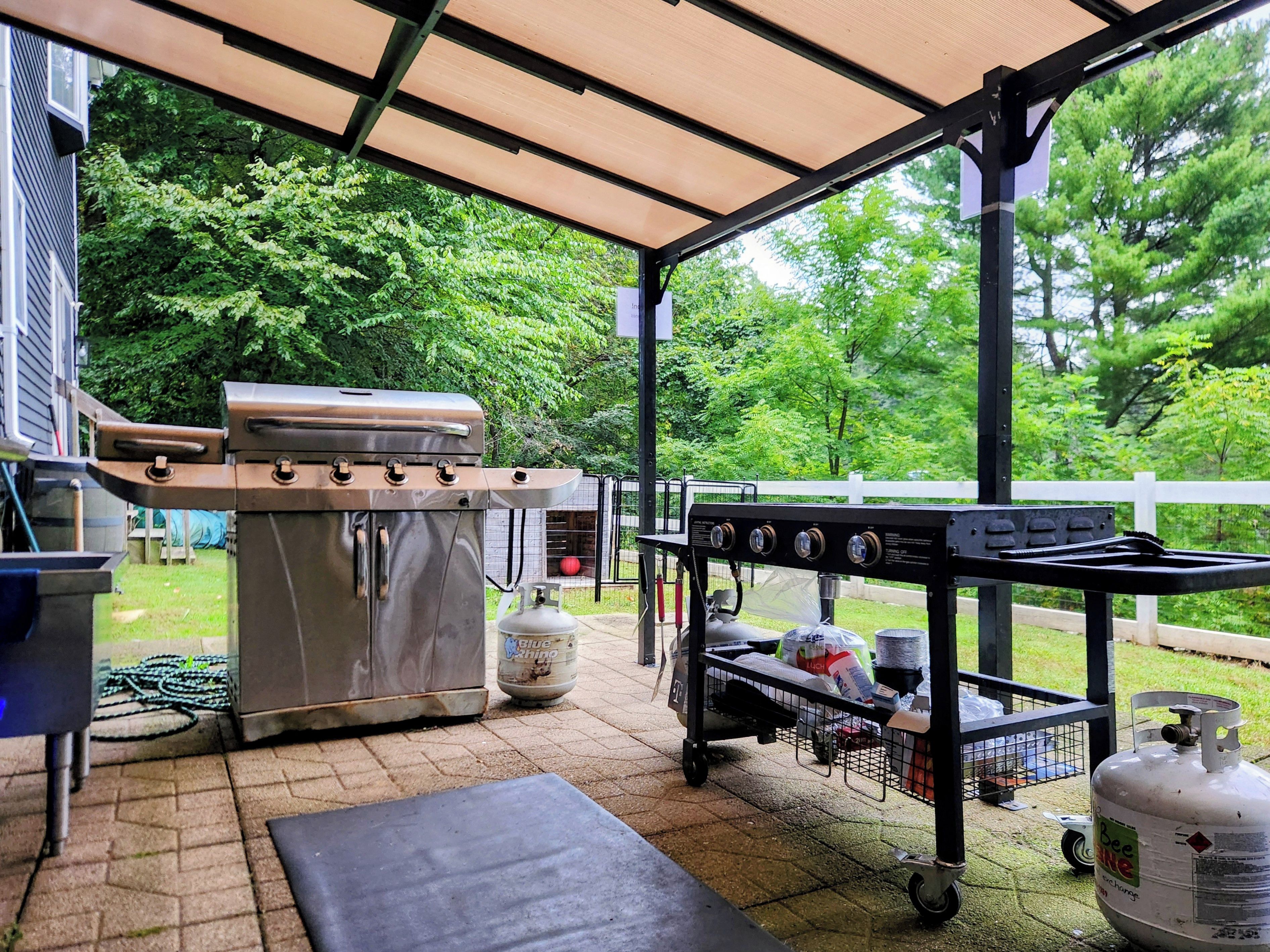 An outdoor patio with a barbecue grill, a gas tank, and a cart with supplies.