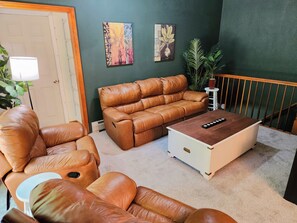 A living room with a brown leather sofa, a white coffee table, and two wall-mounted paintings. - Collinsville River Escape / Fall Foliage, Deck & Yard (Canton)