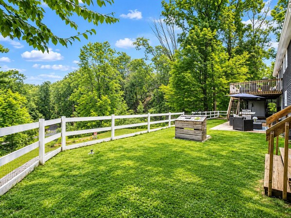 A backyard with a wooden deck, a white fence, and a grill area.