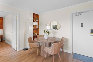 A dining area with a round wooden table, wicker chairs, a vase with flowers, a tall floor lamp, and a wooden bookshelf. - The Golden Jewel • 1BR • Parking • AC • Mins to DT (Edmonton)