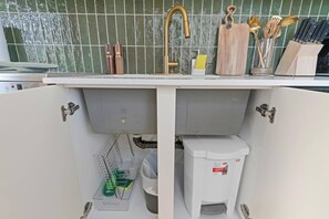 Une cuisine avec un évier blanc, un robinet en acier inoxydable et une poubelle.