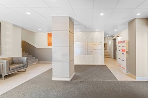 A modern lobby with a reception desk, a staircase, and a row of lockers. - The Golden Jewel • 1BR • Parking • AC • Mins to DT (Edmonton)