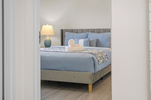 Un dormitori amb un llit, una tauleta de nit, una làmpada i una prestatgeria penjada a la paret.