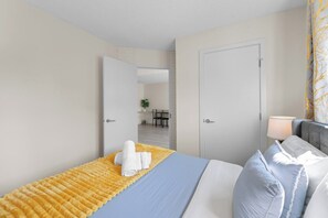 A hotel room with a bed, a bedside table, a chair, and a door leading to a dining area. - The Getaway • 2BR • Parking • AC • Mins to DT (Edmonton)