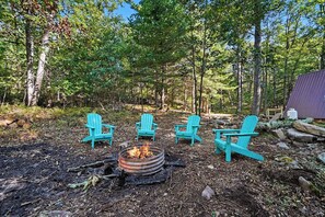 Une zone boisée avec un foyer et quatre chaises Adirondack turquoise disposées autour.