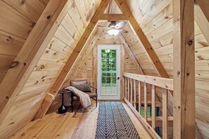 A wooden interior with a sloped ceiling, a door with a grid pattern, a small table with a chair, and a patterned rug.