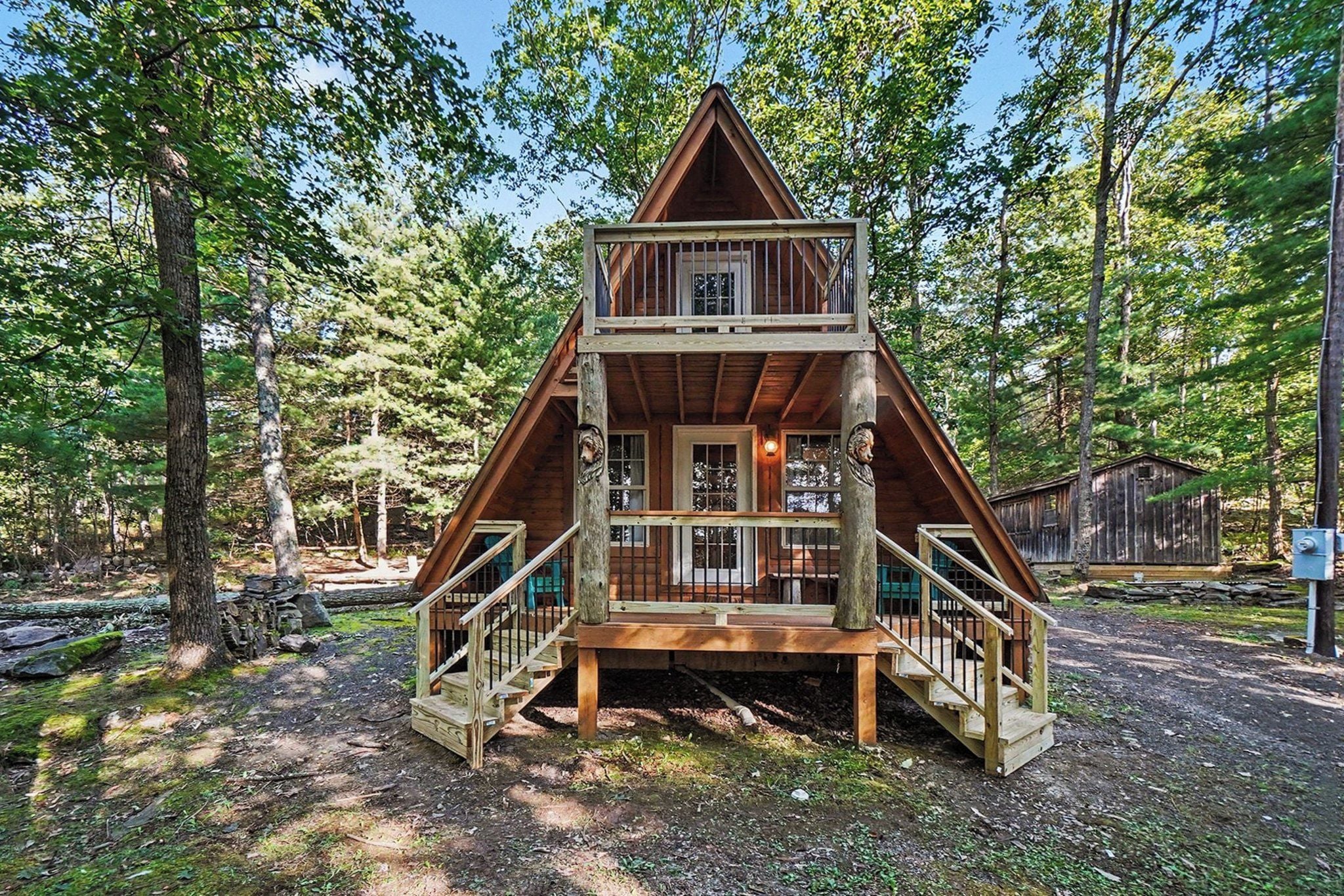 Une cabane en bois dotée d’un balcon et d’un escalier, entourée d’arbres.