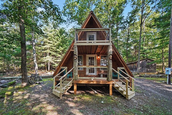 A wooden cabin with a balcony and stairs, surrounded by trees.