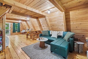 A cozy, wooden interior with a sofa, coffee table, and a dining area.