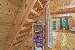 Un intérieur en bois avec un plafond en pente, une étagère remplie de jeux de société et une porte donnant sur l’extérieur.