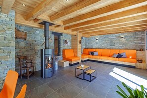 A cozy living room with a stone wall, a fireplace, orange seating, and a tiled floor. - Stunning Luxury Chalet 'MAÉ' (Risoul)
