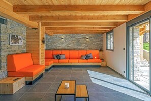A modern interior with a stone wall, wooden ceiling, orange sofa, and a glass door leading outside. - Stunning Luxury Chalet 'MAÉ' (Risoul)