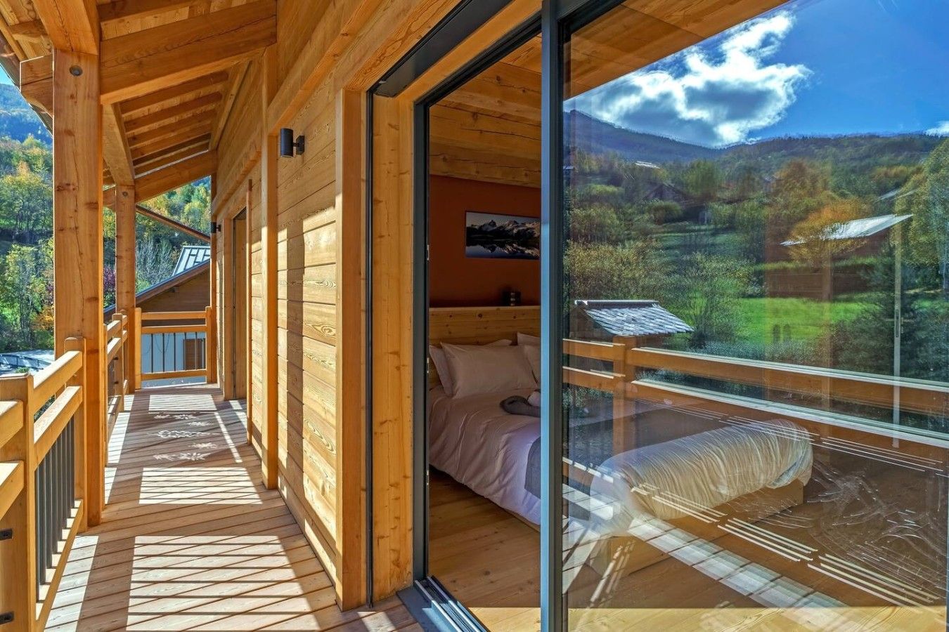A wooden cabin with a balcony, a bed, and a large window offering a view of a forested landscape.