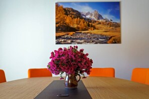 A dining table with a vase of pink flowers, orange chairs, and a painting of a mountain landscape on the wall. - Stunning Luxury Chalet 'MAÉ' (Risoul)