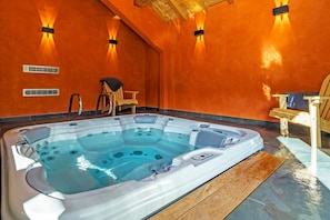 A hot tub in a room with orange walls, wooden ceiling beams, and two chairs. - Stunning Luxury Chalet 'MAÉ' (Risoul)