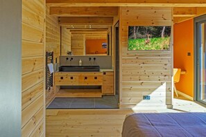 A wooden cabin interior with a central sink, a bed, and a window overlooking greenery. - Stunning Luxury Chalet 'MAÉ' (Risoul)