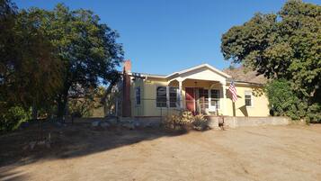 A single-story yellow house with a front porch, a brick chimney, and an American flag.