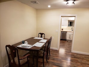 Un comedor con una mesa y sillas de madera, una cocina al fondo y un pasillo que conduce a otra habitación.