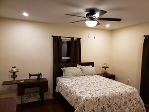 A bedroom with a bed, a desk, a sewing machine, a ceiling fan, and a nightstand with a lamp. - Remodeled 1930s Dehesa Valley Farmhouse, close to Sycuan Casino and more! (El Cajon)