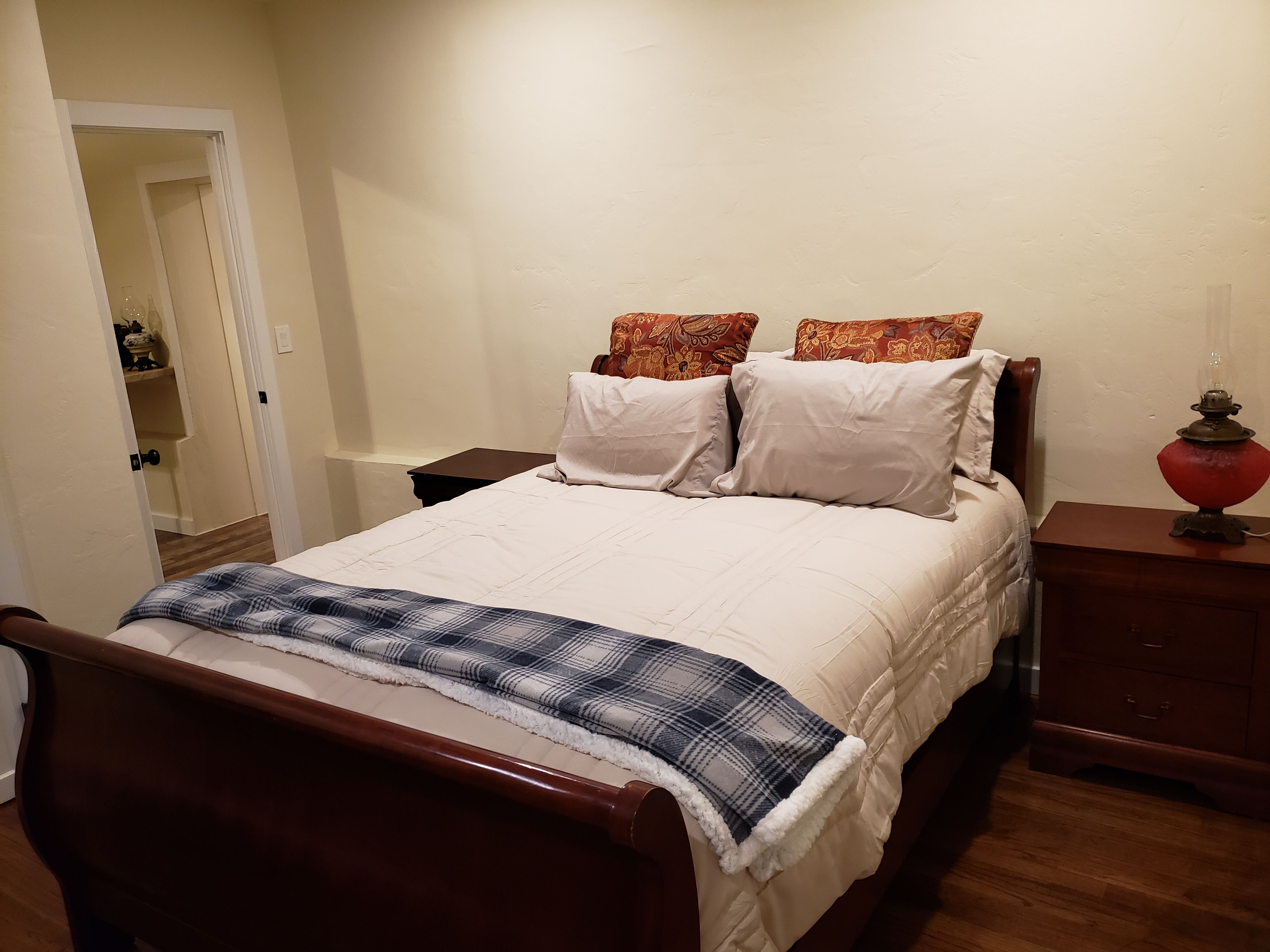 Un letto rifatto con una coperta a quadri, un comodino con una lampada e un piccolo tavolo di legno.