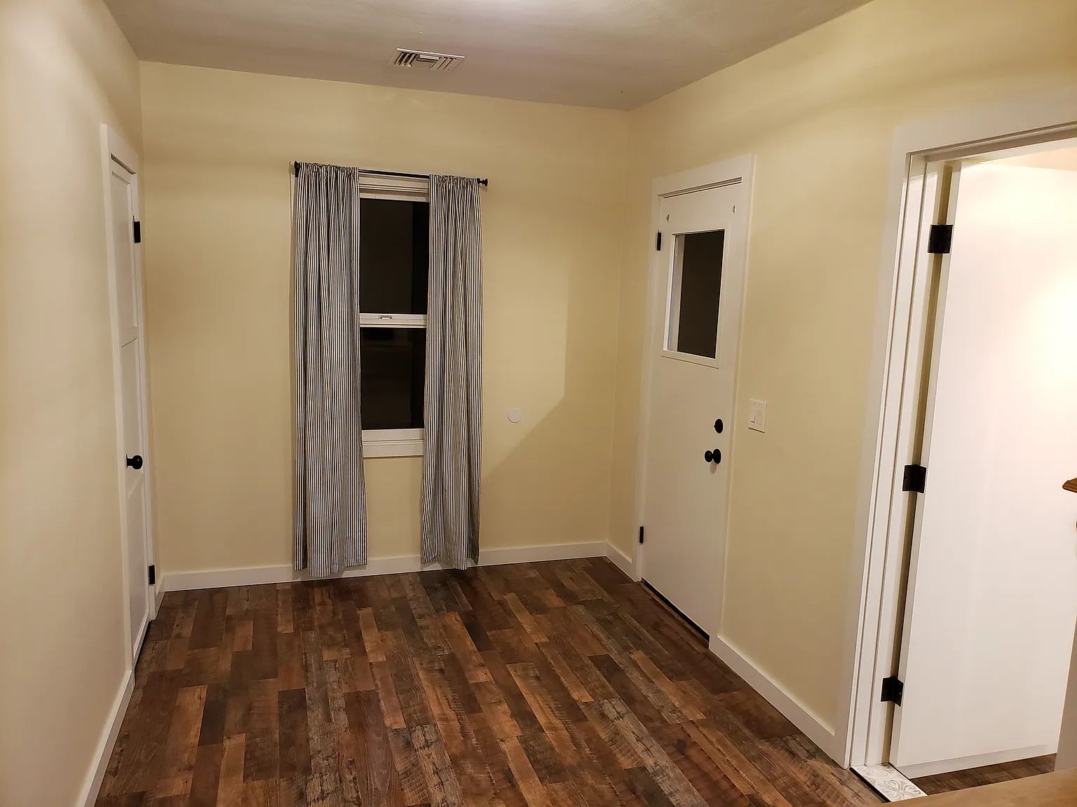 A hallway with wooden flooring, a door with a window, and a curtain.