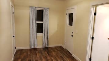 A hallway with wooden flooring, a door with a window, and a curtain.