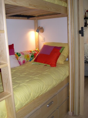 Een stapelbed met een gele matras, een houten hoofdbord en een bedlampje.