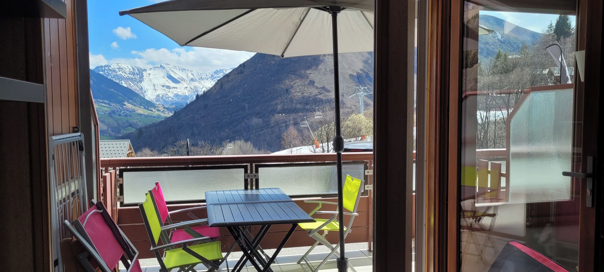 A balcony with a table and chairs, a large umbrella, and a mountain view.