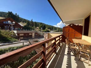 Ein Balkon mit Holzgeländer, einem Tisch mit Stühlen und Blick auf eine Berglandschaft.