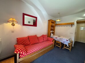 Quarto aconchegante com um sofá vermelho, um armário de madeira e uma mesa com toalha.