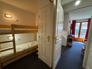Ein Zimmer mit einem Etagenbett, einer Tür, einem kleinen Tisch und Blick ins Freie.