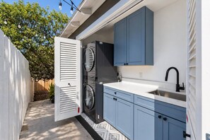 A compact kitchen with a built-in washer and dryer, a sink, and blue cabinets. - Cozy Casa | La Mesa Classic Craftsman (La Mesa)