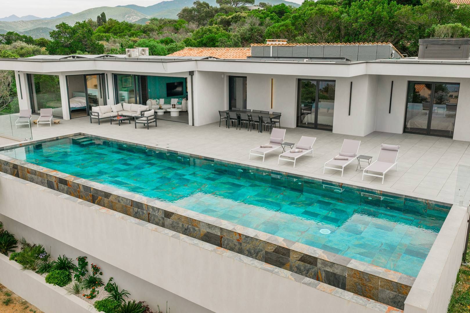 A modern house with a swimming pool, outdoor seating, and a view of the mountains.