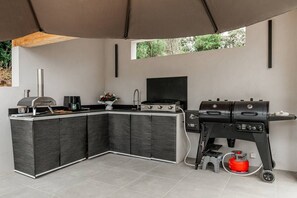 Eine moderne Küche mit integrierter Kochinsel, einem Gasgrill und einem Flachbildfernseher.