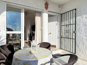 Eine sonnendurchflutete Terrasse mit Tisch und Stühlen, einer Tür und Blick auf die Straße.