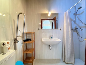 Ein Badezimmer mit Toilette, Waschbecken, Dusche und einem Holzregal.