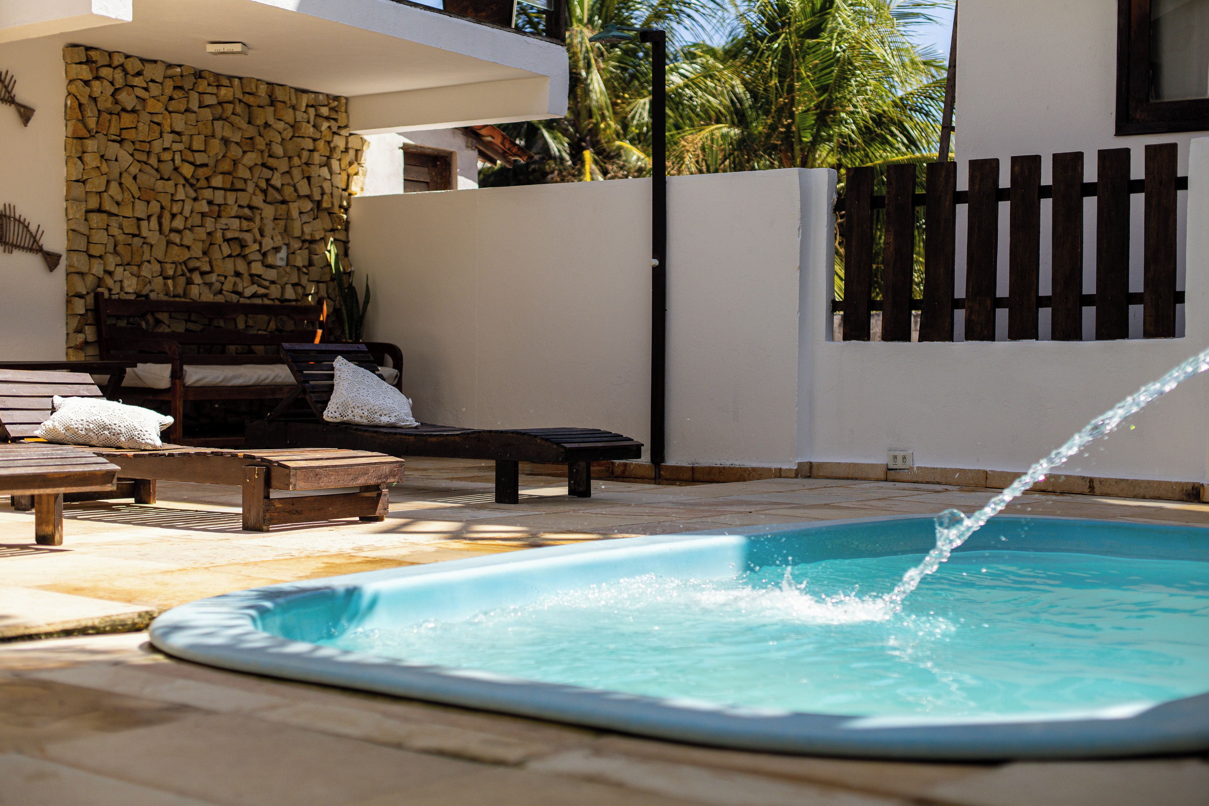 A swimming pool with a wooden deck, lounge chairs, and a stone wall.
