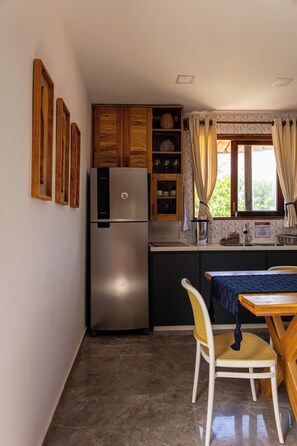 Een compacte keuken met een ingebouwde koelkast, houten kastjes, een eettafel met een stoel en een raam met gordijnen.