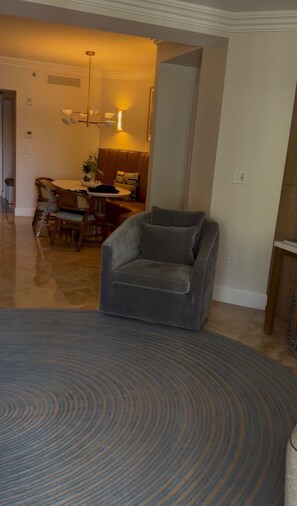 A living room with a grey armchair, a dining area with a table and chairs, and a kitchen in the background. - First-floor 3BR beachfront Lily 4102, Ritz Club Great Bay (Nazareth)