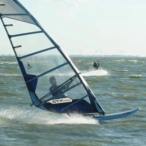 Szene beim Windsurfen, bewölkter Himmel und ruhiges Meer.