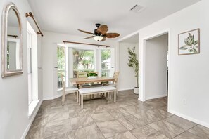 Ein Essbereich mit Holztisch und -stühlen, einem Deckenventilator und großen Fenstern.